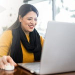 Woman in yellow with black scarf on a laptop.