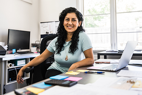 A happy woman posing at her desk in a busy office