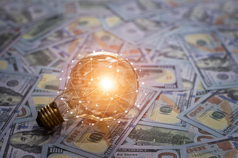 A glowing lightbulb on top of a floor of money