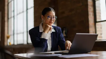 Professional woman in business attire working on a laptop at a desk in a bright, modern office.