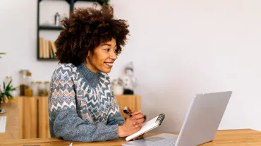 Woman in a sweater sitting at a table looking at a laptop.