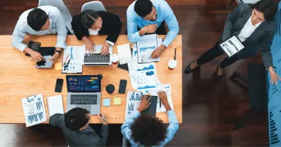 Work team sitting around a table with laptops and documents reviewing data.