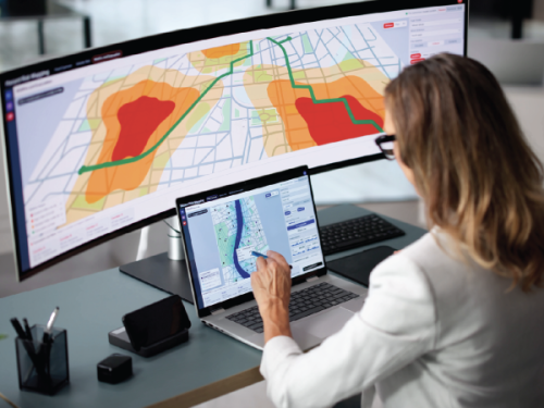 Woman reviewing geographic risk data displayed on a laptop and large monitor.