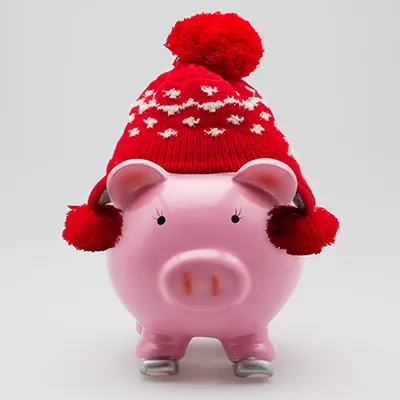 A piggy bank on a gray background wearing a red woolen winter cap