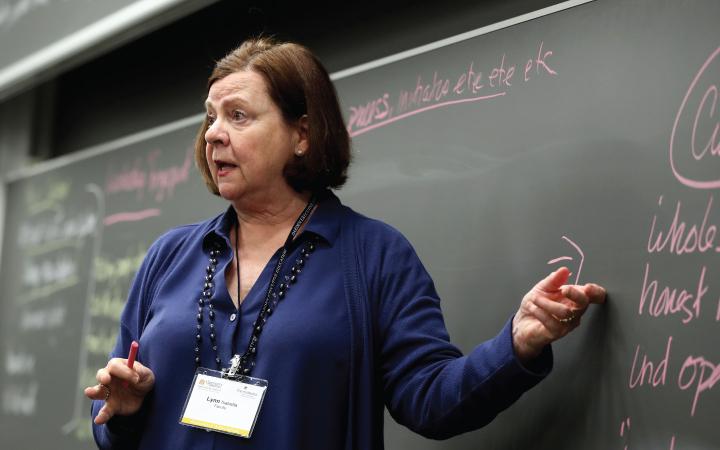 Woman speaking and pointing at chalkboard