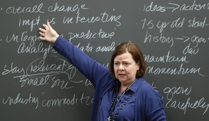 instructor pointing at a chalkboard covered in cursive writing