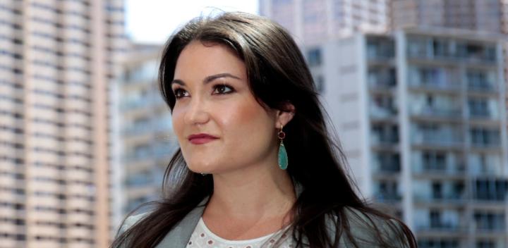 Brown haired woman standing in front of high rise buildings.