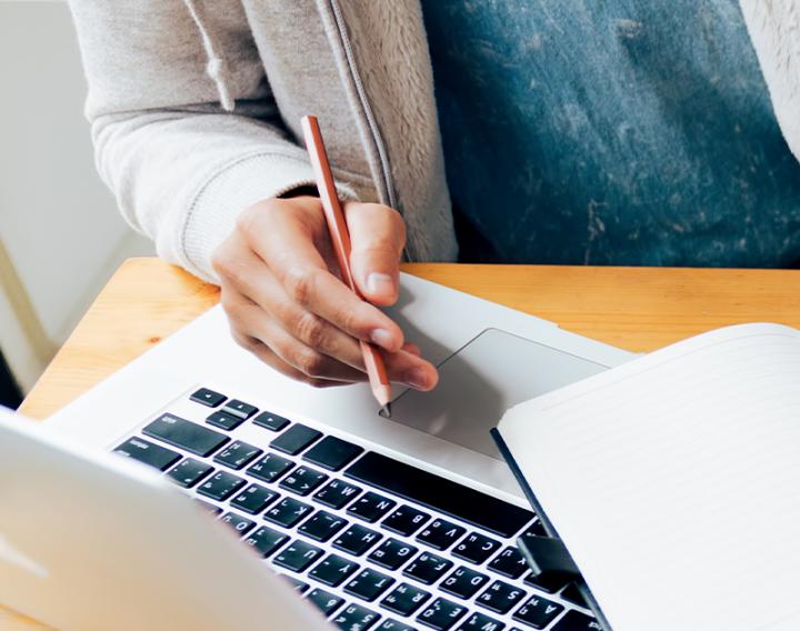 A close up of up laptop and person holding a pencil