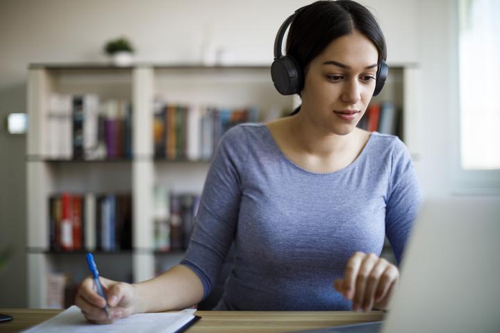 A young woman wearing headphones and working on a laptop learning