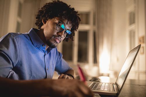 An African American man studying at his laptop in the evening at his home
