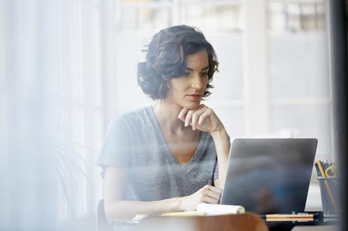 A woman sits at a laptop in concentration