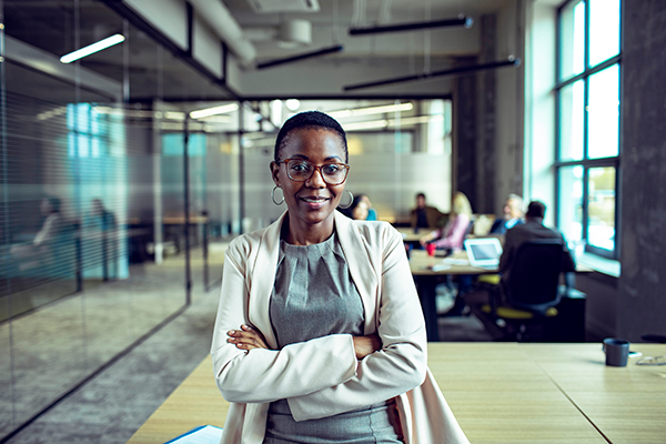 A confident manager stands with her arms crossed in front of her employees