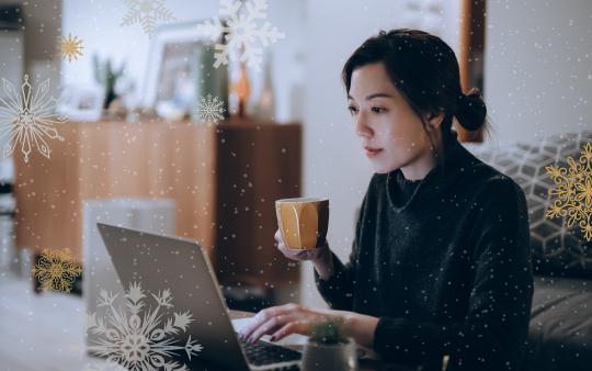 Young woman in black sitting by a laptop with mug.