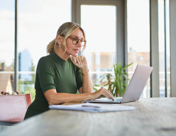 Women in glasses and green top sitting at a table on a laptop.