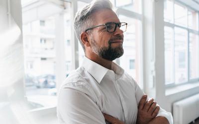 Man with glasses and beard in a white shirt with arm crossed smiling and looking confident