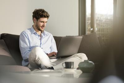A man sitting cross-legged on a couch studying on a laptop