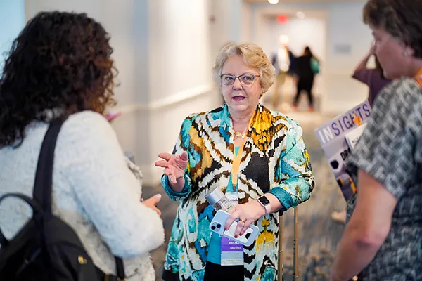 Carol Blaine standing and talking to attendees at In2Leadership